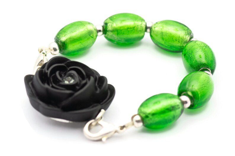 May include: A black fabric rose charm bracelet with green glass beads. The bracelet has a silver clasp.