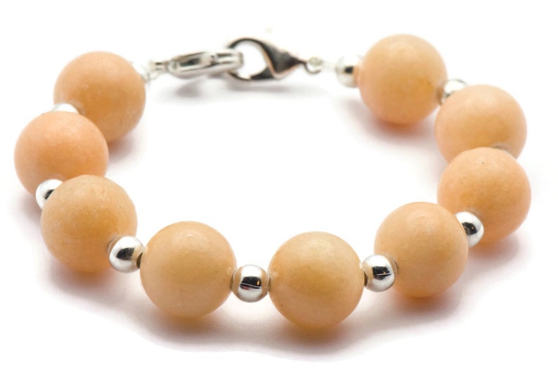 Puede incluir: Un brazalete hecho de cuentas redondas de color melocot&oacute;n con detalles plateados.
