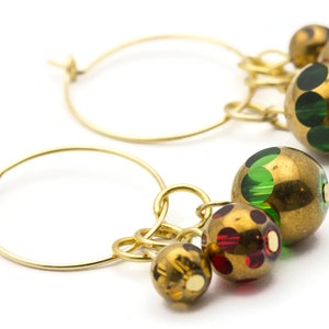 Puede incluir: Aretes de aro de oro con colgantes. Los colgantes son redondos y tienen un acabado dorado con lunares verdes y rojos.