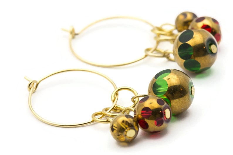 Puede incluir: Aretes de aro de oro con colgantes. Los colgantes son redondos y tienen un acabado dorado con lunares verdes y rojos.