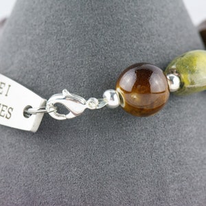 May include: A silver bracelet with a tag that reads "Type 1 Diabetes". The bracelet is made with brown and green ceramic beads and a silver clasp.