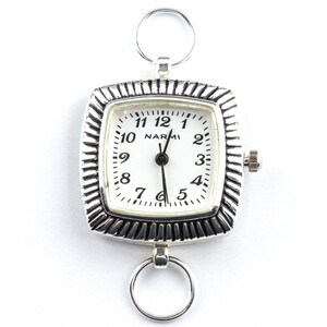 May include: A silver pocket watch with a square face and a white dial. The watch has a textured bezel and a small crown. The dial features black numerals and the brand name "NARMI". Two silver rings are attached to the top and bottom of the watch.
