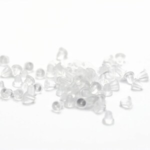 May include: A pile of clear plastic earring backs. The backs are small and round, with a slight lip around the edge.