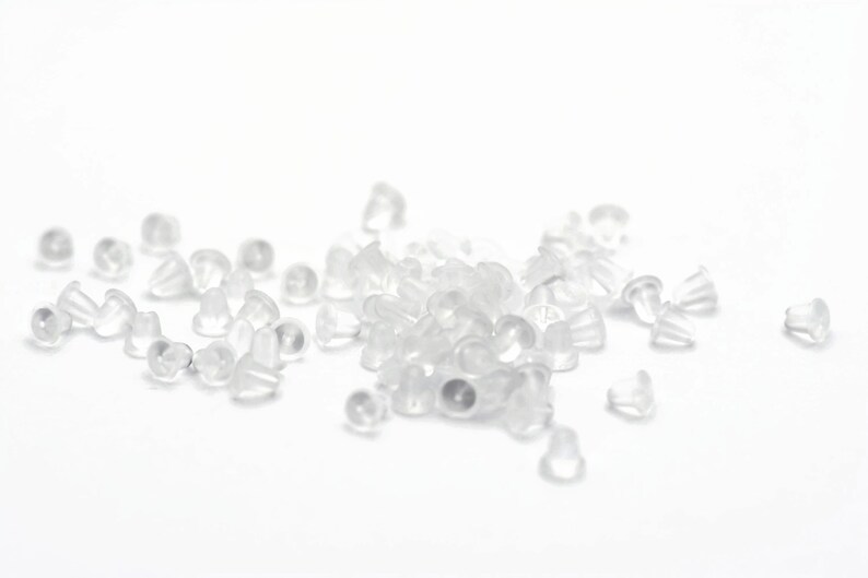 May include: A pile of clear plastic earring backs. The backs are small and round, with a slight lip around the edge.