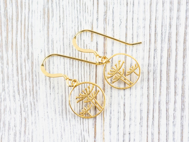 May include: A pair of gold dangle earrings with a delicate design of three stylized flowers in a circle.