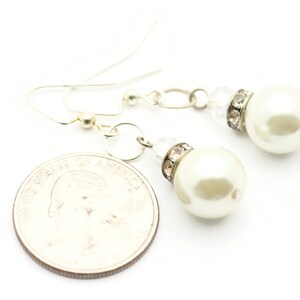 Peut inclure: Une paire de boucles d'oreilles pendantes argent&eacute;es avec des perles blanches et des accents de strass transparents.
