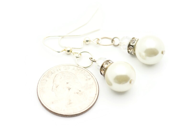 Peut inclure: Une paire de boucles d'oreilles pendantes argent&eacute;es avec des perles blanches et des accents de strass transparents.