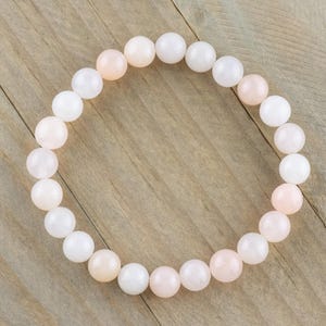 Op de afbeelding: Een armband gemaakt van witte en roze ronde kralen. De armband is gemaakt van natuursteen en is ongeveer 18 cm lang.