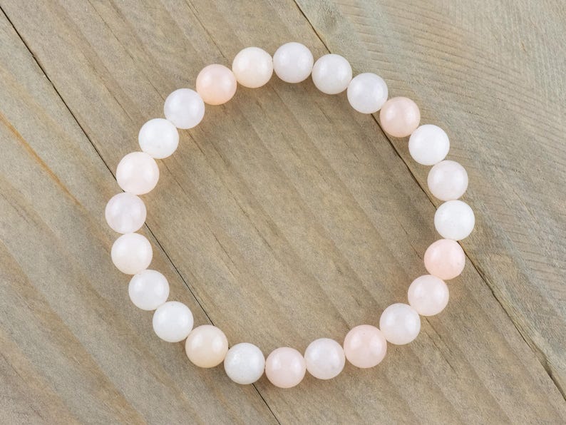 Op de afbeelding: Een armband gemaakt van witte en roze ronde kralen. De armband is gemaakt van natuursteen en is ongeveer 18 cm lang.
