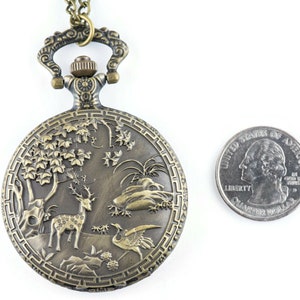 Pu&ograve; includere: Un orologio da tasca in bronzo con una catena, che presenta un design inciso di un cervo, un uccello e un albero. L'orologio &egrave; circa delle dimensioni di una moneta da 25 centesimi.