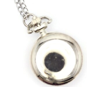 Op de afbeelding: Een zilveren zakhorloge met een ketting eraan. De wijzerplaat van het horloge is niet zichtbaar.