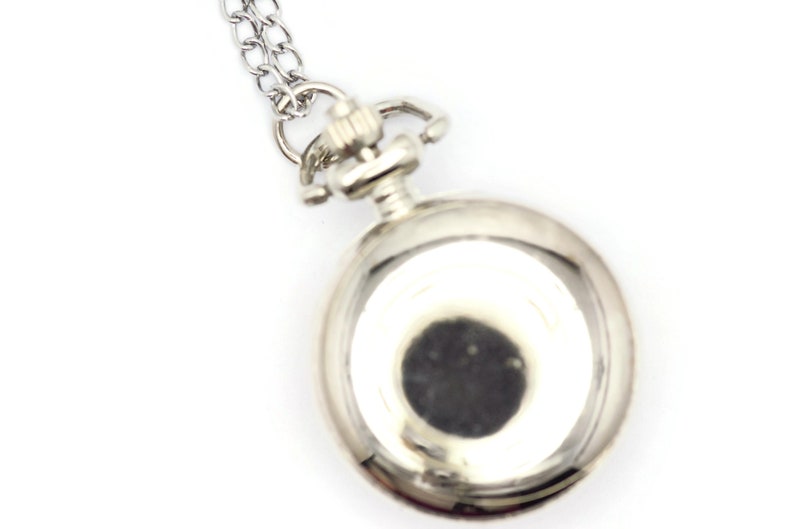Op de afbeelding: Een zilveren zakhorloge met een ketting eraan. De wijzerplaat van het horloge is niet zichtbaar.