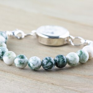 May include: A silver watch with a white face and a green and white agate bead bracelet.