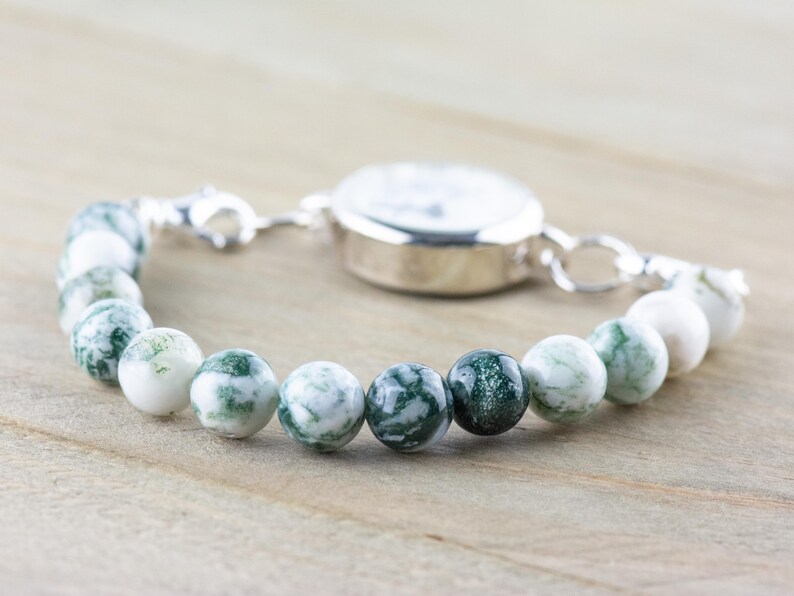 May include: A silver watch with a white face and a green and white agate bead bracelet.