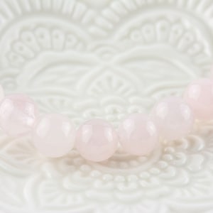 May include: A pink rose quartz bracelet with round beads. The bracelet is on a white background with a floral design.