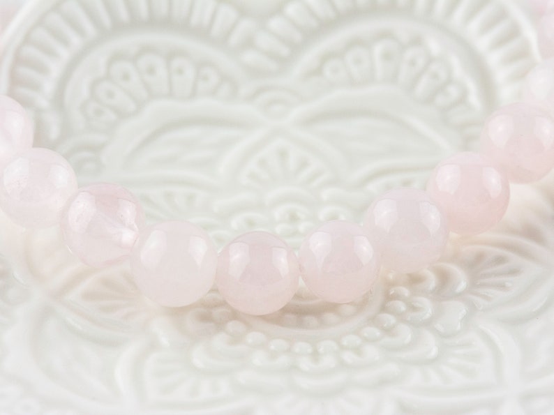 May include: A pink rose quartz bracelet with round beads. The bracelet is on a white background with a floral design.
