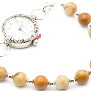 May include: A silver watch with a white face and black hands attached to a brown and white beaded bracelet.