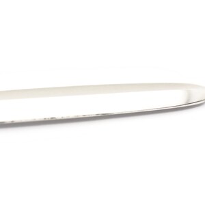 Puede incluir: Un cuchillo de mantequilla de plata con una punta redondeada y una superficie lisa y pulida.