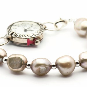 Peut inclure: Une montre argent&eacute;e avec un cadran blanc et des aiguilles noires est attach&eacute;e &agrave; un bracelet compos&eacute; de perles brun clair et de perles argent&eacute;es.