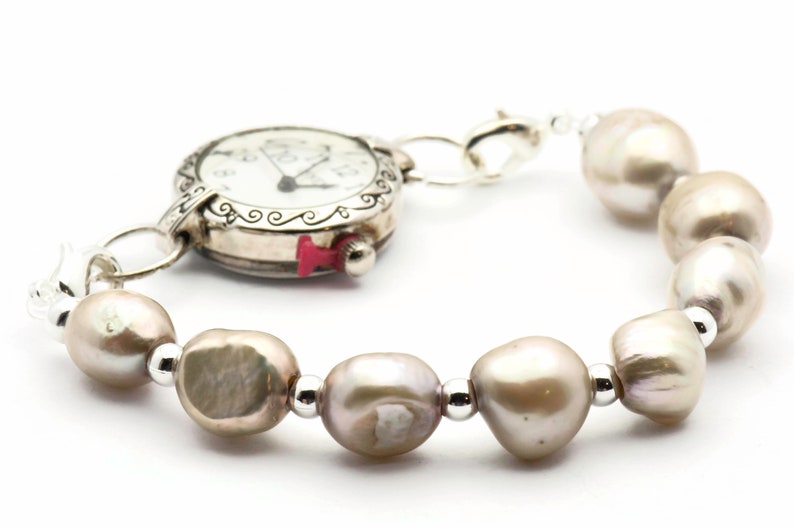Peut inclure: Une montre argent&eacute;e avec un cadran blanc et des aiguilles noires est attach&eacute;e &agrave; un bracelet compos&eacute; de perles brun clair et de perles argent&eacute;es.
