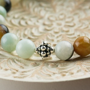 Black Gold Amazonite Genuine Gemstone Stretch Bracelet displayed on a decorative bowl. Amazonite beads are multicolor earth-tones. Close up of center bead is a silver Bali style bead.