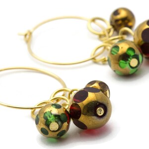 May include: Gold hoop earrings with dangling charms. The charms are round and have a gold finish with green and red patterned glass.