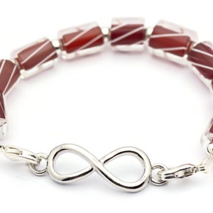 K&ouml;nnte beinhalten: Ein Armband aus roten und wei&szlig;en, gestreiften Glasperlen mit einem Unendlichkeits-Anh&auml;nger. Das Armband ist aus Silber und hat einen Verschluss.