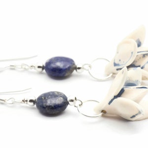 May include: A pair of silver earrings with blue lapis lazuli stones and white ceramic flower charms.