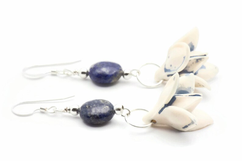 May include: A pair of silver earrings with blue lapis lazuli stones and white ceramic flower charms.