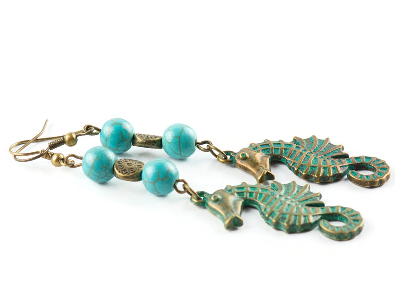 May include: A pair of turquoise and bronze earrings featuring seahorse charms and turquoise beads.