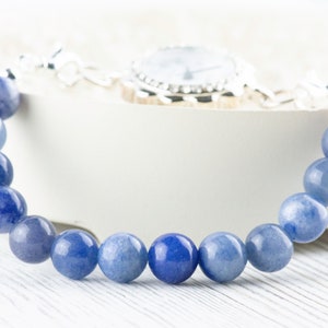 May include: A blue gemstone bracelet with a silver watch clasp. The bracelet is made of round, smooth beads.