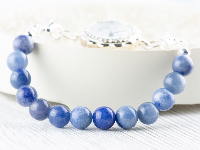 May include: A blue gemstone bracelet with a silver watch clasp. The bracelet is made of round, smooth beads.