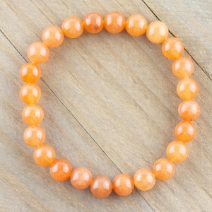 May include: A bracelet made of orange carnelian beads. The beads are round and smooth, and the bracelet is strung on a clear elastic cord.