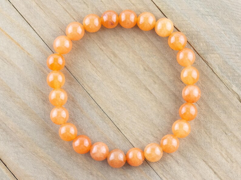 May include: A bracelet made of orange carnelian beads. The beads are round and smooth, and the bracelet is strung on a clear elastic cord.