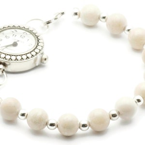 Op de afbeelding: Een zilveren horloge met een witte wijzerplaat en zwarte wijzers is bevestigd aan een armband gemaakt van witte kralen en zilveren tussenstukken.