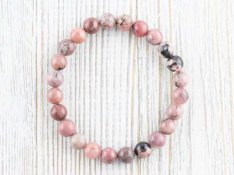 May include: A pink and black gemstone bracelet with round beads. The bracelet is made of natural stones and is strung on a clear elastic cord.