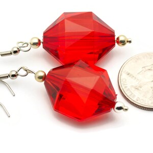 May include: A pair of red faceted glass earrings with silver hooks and gold accents. The earrings are shown next to a US quarter for size reference.