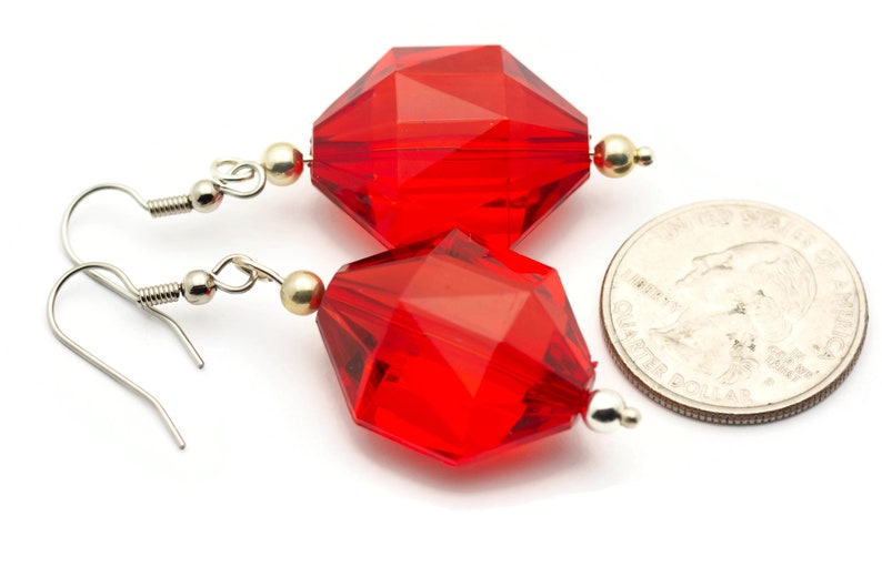 May include: A pair of red faceted glass earrings with silver hooks and gold accents. The earrings are shown next to a US quarter for size reference.
