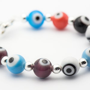 Puede incluir: Un brazalete con un cierre plateado y cuentas de colores con dise&ntilde;os de ojo turco. Las cuentas son azules, rojas, blancas, negras y moradas.