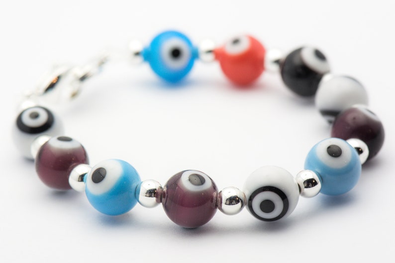 Puede incluir: Un brazalete con un cierre plateado y cuentas de colores con dise&ntilde;os de ojo turco. Las cuentas son azules, rojas, blancas, negras y moradas.