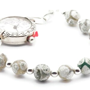 Op de afbeelding: Een zilveren horloge met een witte wijzerplaat en zwarte wijzers bevestigd aan een armband gemaakt van witte en groene agaat kralen.