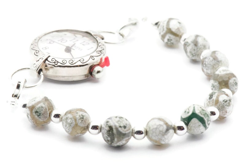 Op de afbeelding: Een zilveren horloge met een witte wijzerplaat en zwarte wijzers bevestigd aan een armband gemaakt van witte en groene agaat kralen.