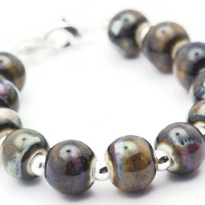 May include: A bracelet made of dark brown ceramic beads with silver accents. The beads have a mottled, iridescent finish.