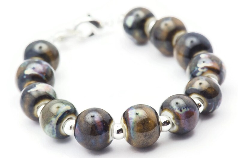 May include: A bracelet made of dark brown ceramic beads with silver accents. The beads have a mottled, iridescent finish.