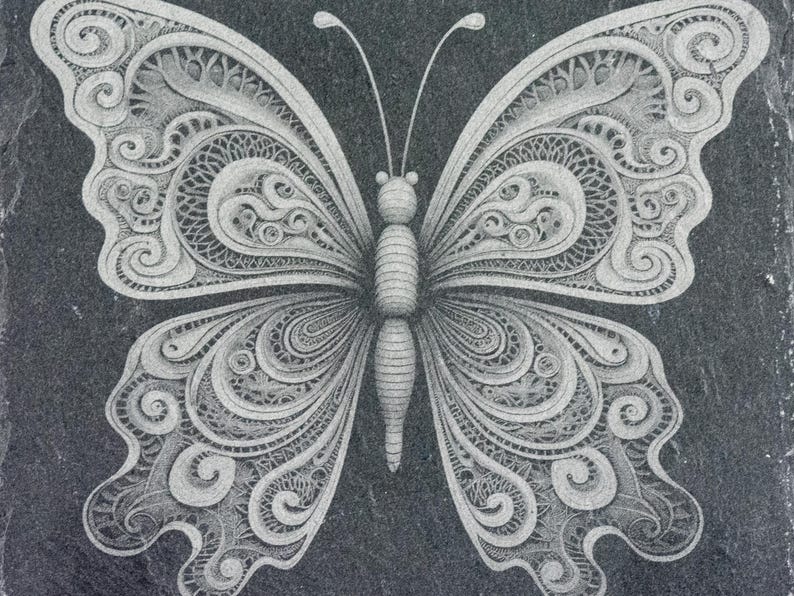 May include: A detailed, intricate, white butterfly design carved into a black slate surface.