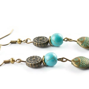May include: A pair of bronze earrings with turquoise beads and fish charms. The earrings have a hook closure.