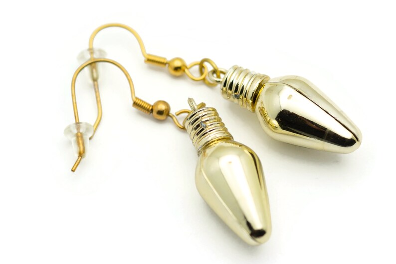 Puede incluir: Un par de pendientes de color dorado con forma de bombilla. Los pendientes tienen un dise&ntilde;o sencillo y elegante, perfectos para a&ntilde;adir un toque de brillo a cualquier atuendo.