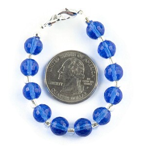 Pu&ograve; includere: Un braccialetto di perline di cristallo blu con chiusura argentata. Il braccialetto &egrave; circa delle dimensioni di una moneta da 25 centesimi di dollaro americano.
