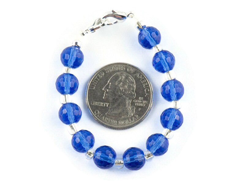 Pu&ograve; includere: Un braccialetto di perline di cristallo blu con chiusura argentata. Il braccialetto &egrave; circa delle dimensioni di una moneta da 25 centesimi di dollaro americano.
