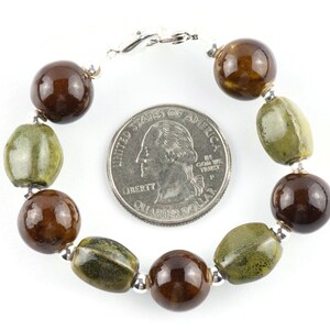 May include: A brown and green ceramic bead bracelet with a silver clasp. The bracelet is about the size of a quarter.